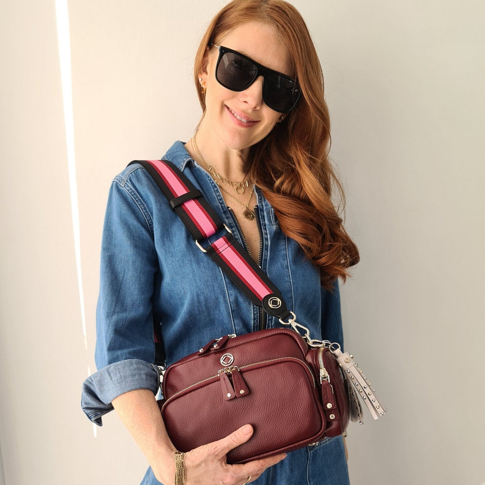model wearing webster black berry pink stripe leather bag strap attached to greta oxblood leather cross body bag