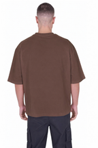 A man viewed from the back wearing an oversized brown short-sleeve t-shirt and dark cargo pants against a plain white background.