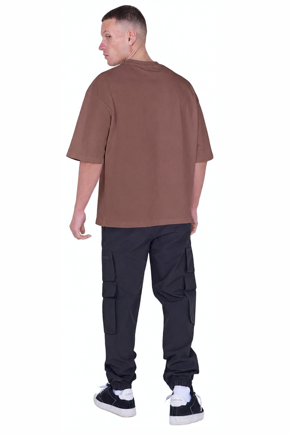 A man shown from the back wearing an oversized brown t-shirt, black cargo pants, and black and white sneakers, set against a plain white background.