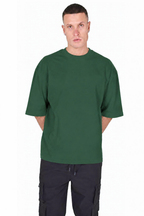 A man wearing an oversized dark green short-sleeve t-shirt and dark cargo pants, standing against a plain white background.