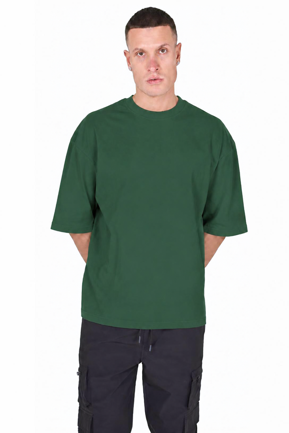 A man wearing an oversized dark green short-sleeve t-shirt and dark cargo pants, standing against a plain white background.