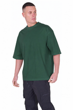 A man wearing an oversized dark green short-sleeve t-shirt and dark cargo pants, standing against a plain white background.