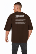A man viewed from the back wearing a dark brown t-shirt with white printed text on the upper back reading 'FOREVER FORWARD FOREVER GRATEFUL' and smaller text below, paired with dark gray jeans against a plain white background.