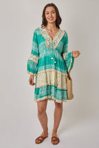 Woman wearing a green and beige patterned dress holding a straw bag on a white background