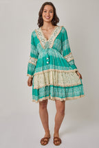Woman wearing a teal and beige dress with lace details on a plain background