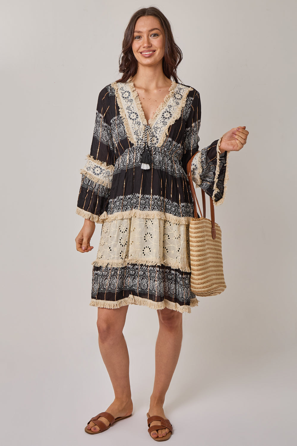 Woman wearing a black and white patterned dress holding a bag on a plain background