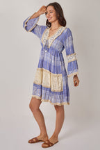Woman wearing a blue and white patterned dress with lace details on a plain background