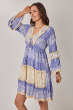 Woman wearing a blue and white patterned dress with lace details on a plain background