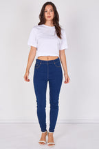 A woman modeling a white cropped short-sleeve t-shirt and dark blue skinny jeans against a plain white studio background.