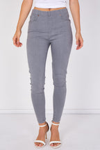 A model wearing high-waisted, light gray skinny jeans with a white crop top and white heeled sandals, shown from the waist down against a white studio background.