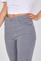 Close-up of a person wearing light gray slim-fit jeans with a white cropped t-shirt, showing the waistband, front pockets, and hand resting on the hip against a plain light background.