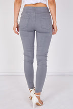 A person shown from the back wearing light gray slim-fit skinny jeans with white heeled sandals against a plain white studio background.