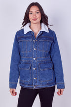 A woman modeling a blue denim jacket with a contrasting white sherpa collar, paired with black pants, against a light gray studio background.
