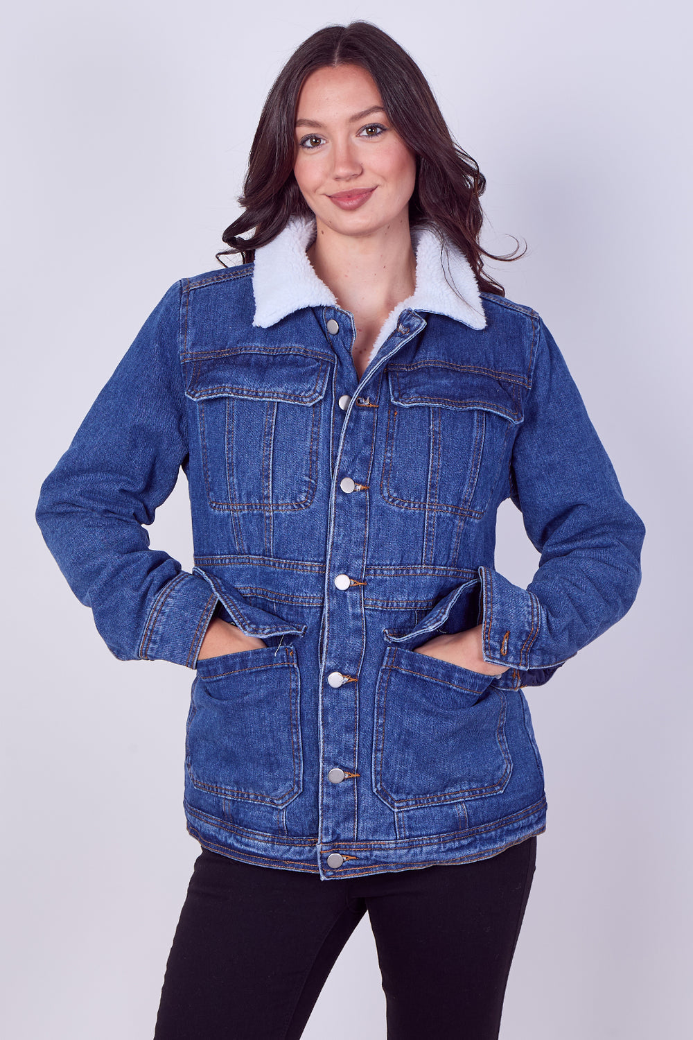 A woman modeling a blue denim jacket with a white sherpa collar, standing against a light gray studio background.