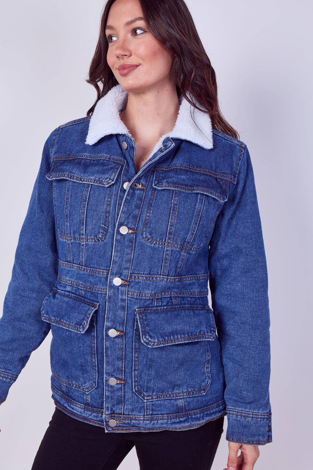 A woman wearing a blue denim jacket with a white sherpa collar, photographed against a light gray studio background.
