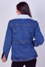A woman viewed from the back wearing a blue denim jacket with a white sherpa collar, paired with black pants, against a light gray studio background.