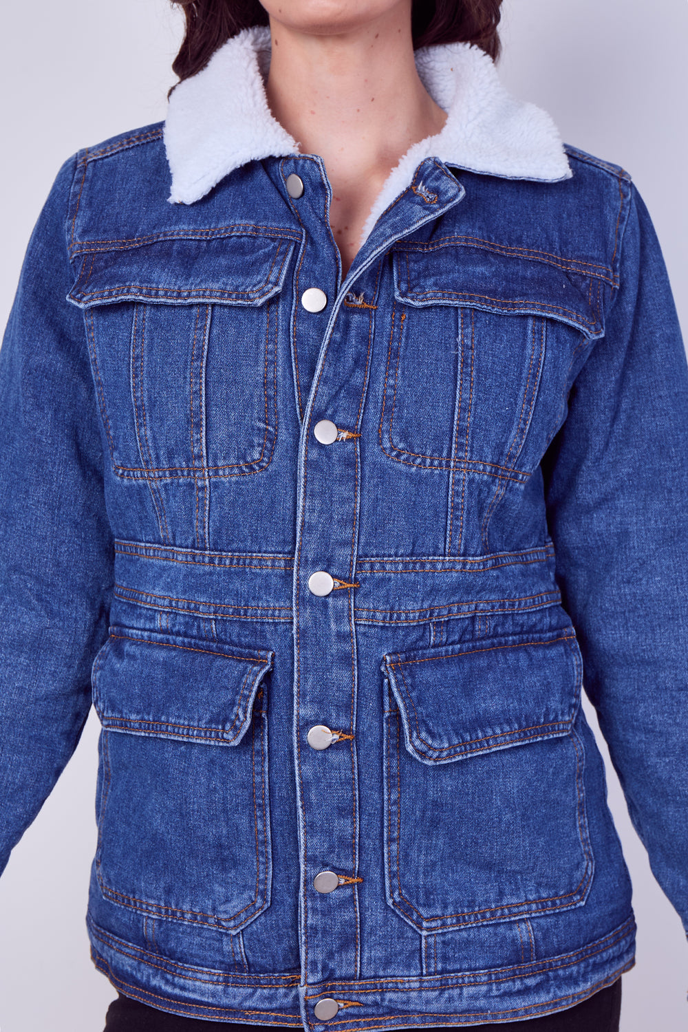 A blue denim jacket with a white sherpa fleece collar, featuring front button closure, chest flap pockets, and lower patch pockets, shown on a model against a light gray background.