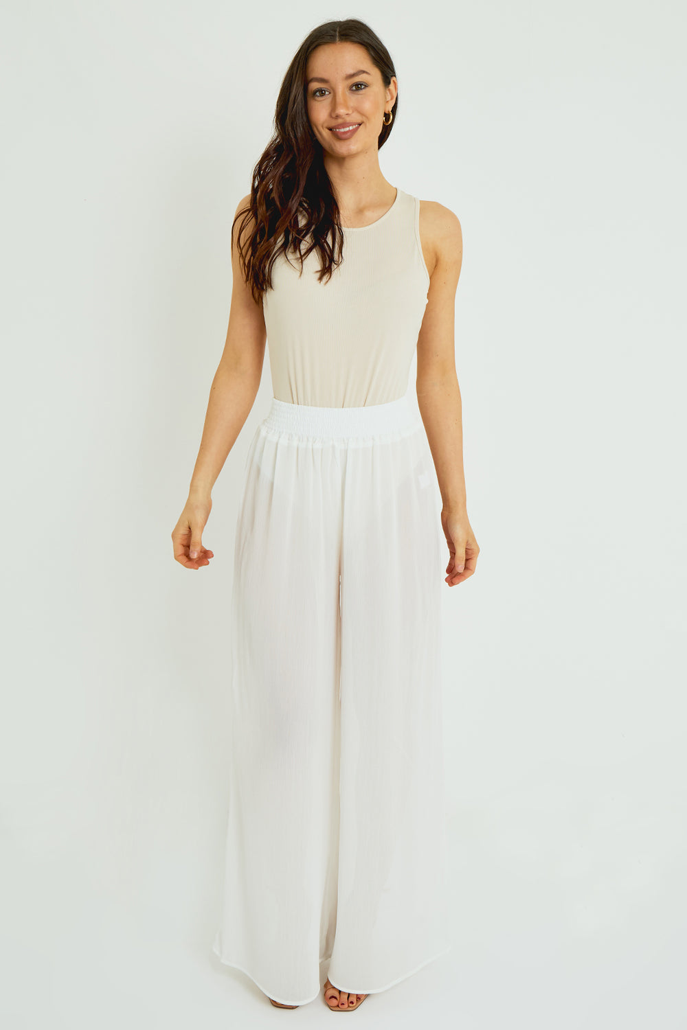 Woman wearing a sleeveless beige top and white flowing skirt on a white background