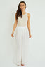 Woman wearing a sleeveless beige top and white flowing skirt on a white background