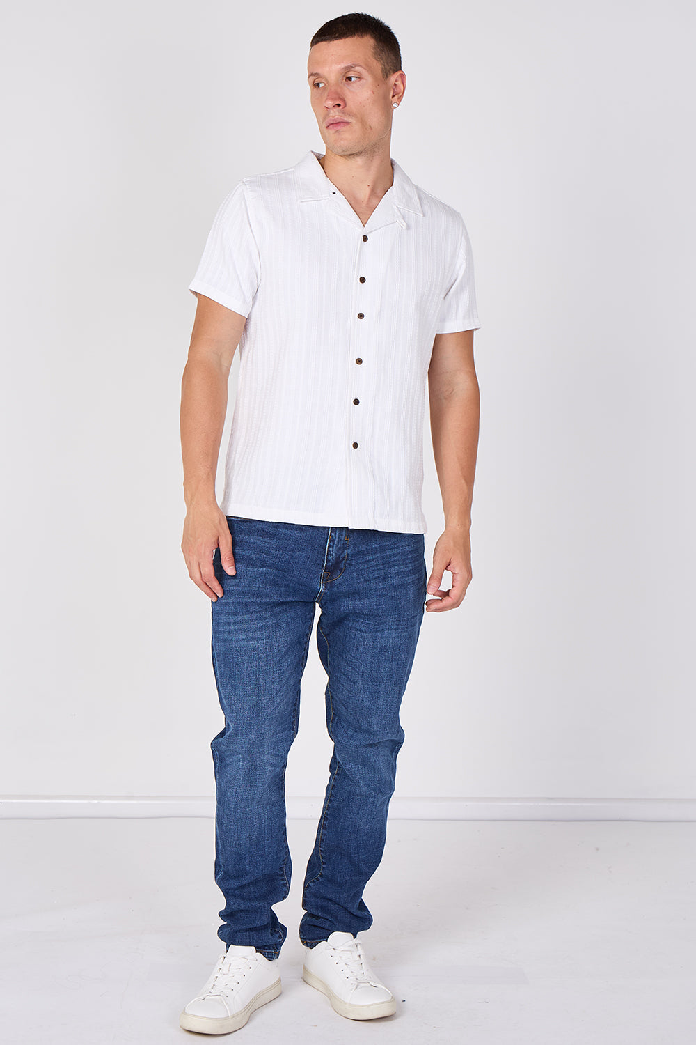 A man modeling a white short-sleeve button-up shirt with subtle vertical stripes, paired with blue jeans and white sneakers, against a plain white studio background. Main image