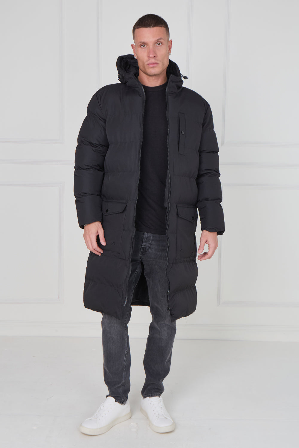 Man wearing a long black puffer coat against a white background