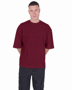 A man wearing an oversized short-sleeve crewneck t-shirt in maroon and dark cargo pants, standing against a plain white background.