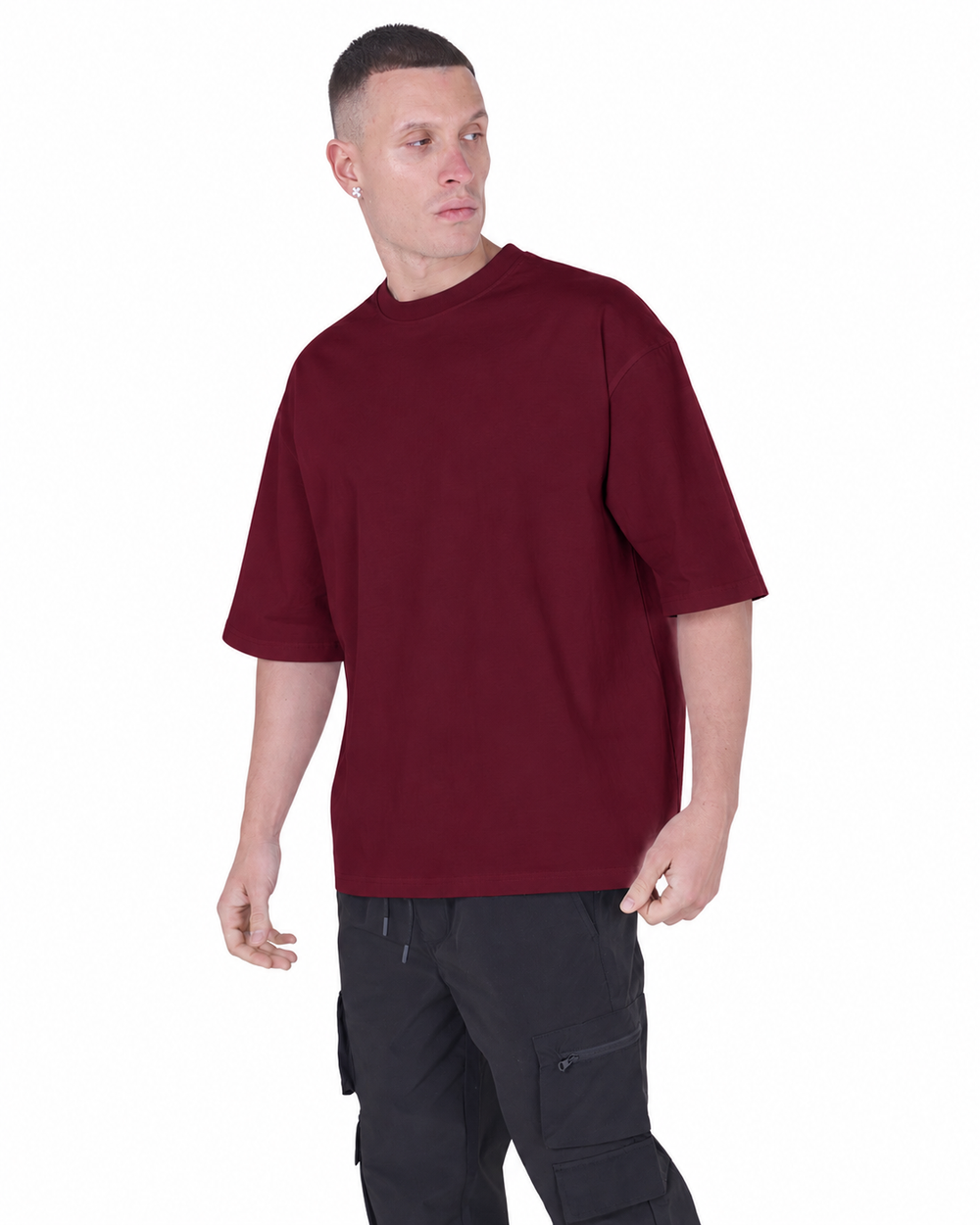 A man wearing an oversized short-sleeve crewneck t-shirt in deep burgundy, paired with black cargo pants, photographed against a solid white background.