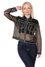 Woman wearing a black sheer jacket over a black top with dark jeans on a beige background