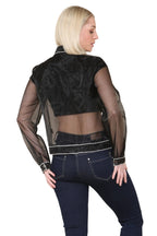 Woman wearing a black sheer jacket over a black top and blue jeans on a beige background
