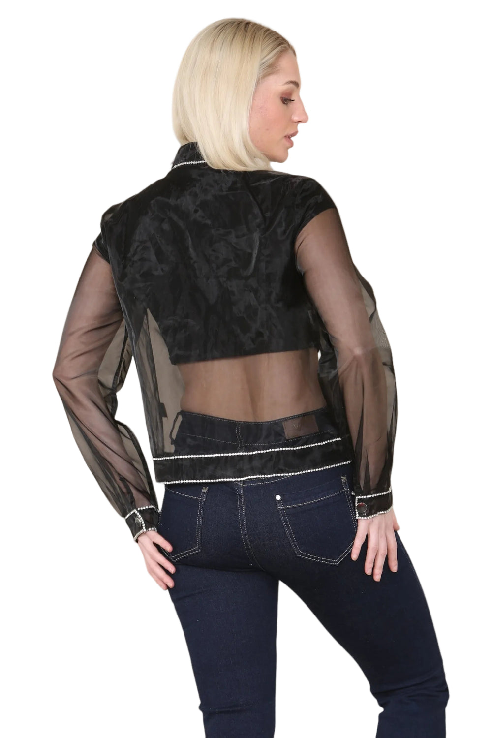 Woman wearing a black sheer jacket over a black top and blue jeans on a beige background