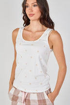 Woman wearing a white tank top with small gold patterns on a plain background