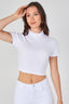 Woman wearing a white crop top and white pants against a plain background