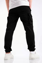 Black cargo jogger pants with side flap pockets and elastic cuffs, shown on a model from the back wearing a white t-shirt and white sneakers.