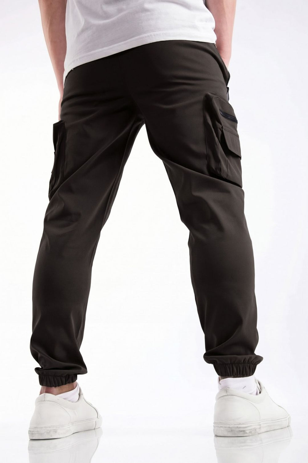 Black cargo jogger pants with side flap pockets and elastic cuffs, shown on a model from the back wearing a white t-shirt and white sneakers.
