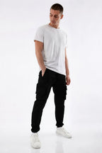 A man modeling black cargo pants with a white t-shirt and white sneakers against a plain white studio background.