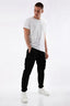 A man modeling black cargo pants with a white t-shirt and white sneakers against a plain white studio background.