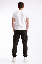 A man viewed from behind wearing a white t-shirt, black cargo pants, and white sneakers against a plain white studio background.