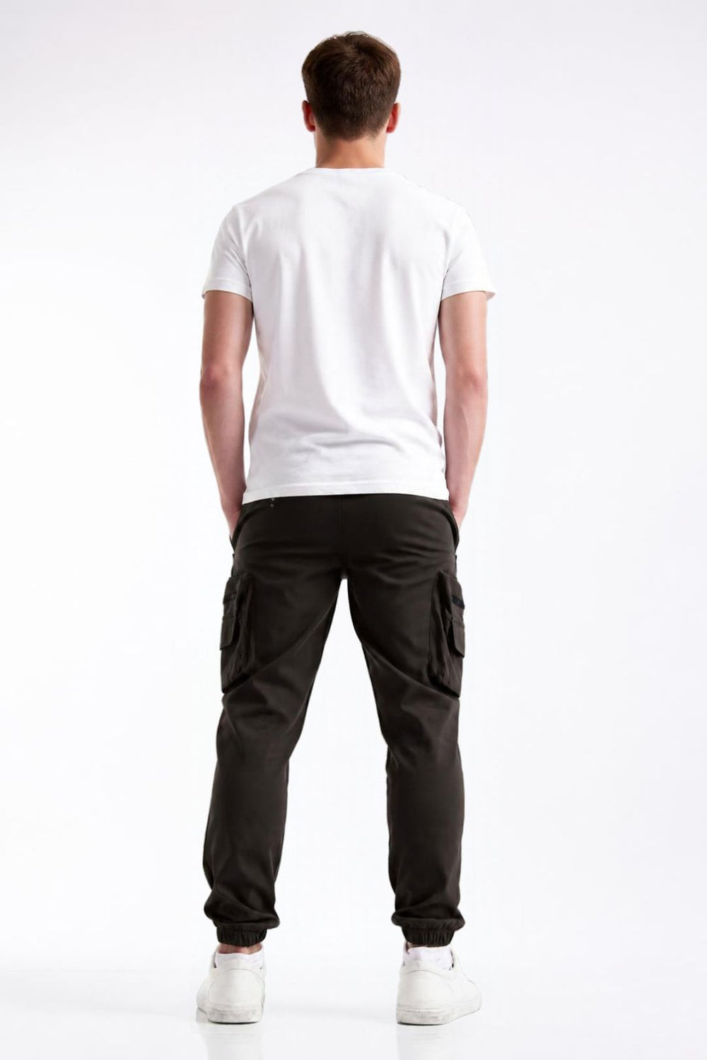 A man viewed from behind wearing a white t-shirt, black cargo pants, and white sneakers against a plain white studio background.