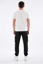 A man viewed from the back wearing a plain white short-sleeve t-shirt, black cargo pants, and white sneakers, standing against a seamless white studio background.