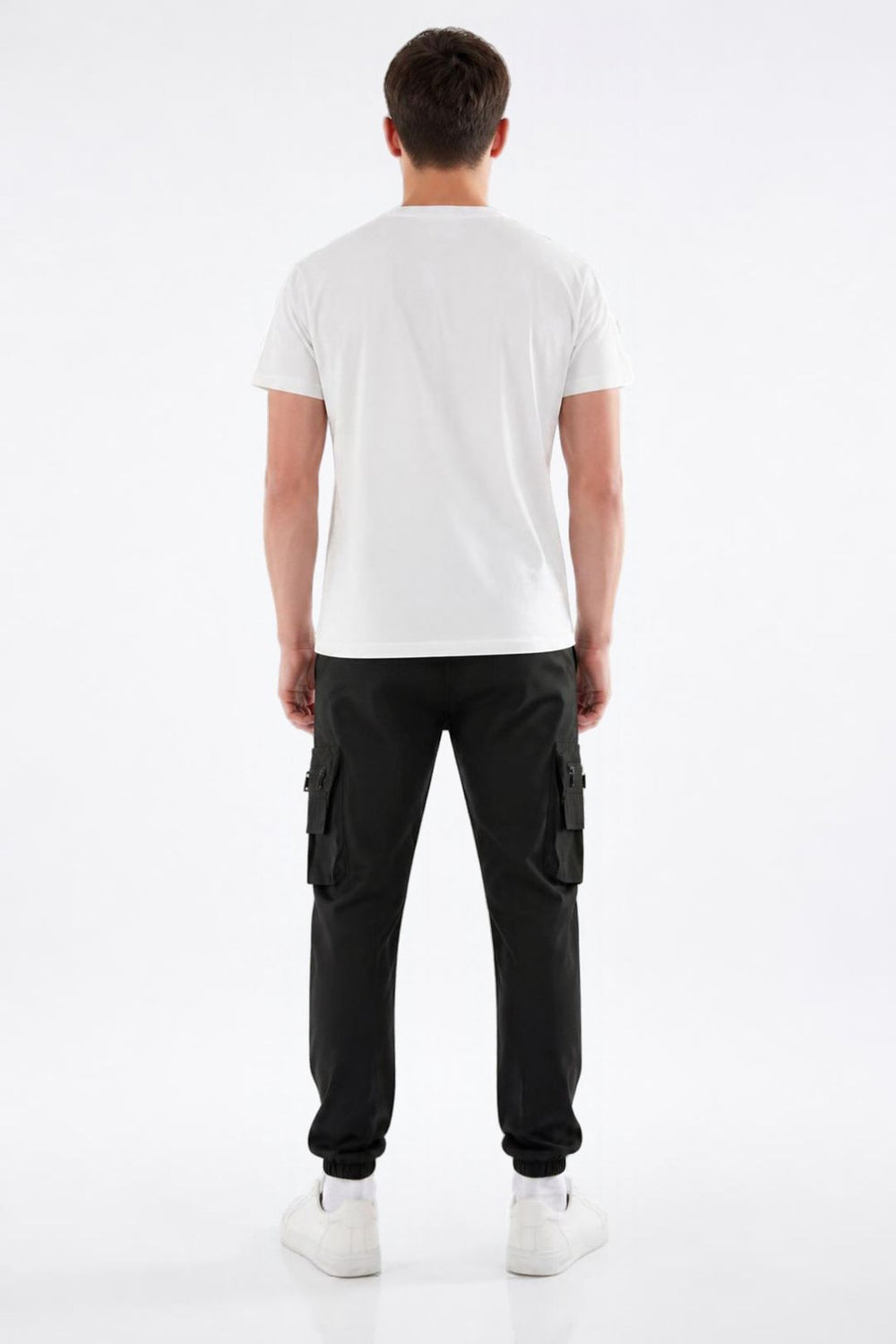 A man viewed from the back wearing a plain white short-sleeve t-shirt, black cargo pants, and white sneakers, standing against a seamless white studio background.